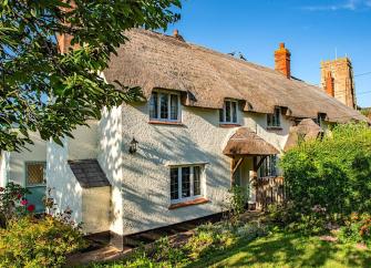 Exterior of a semi-detached thatched cottage overlooking a lawned garden.