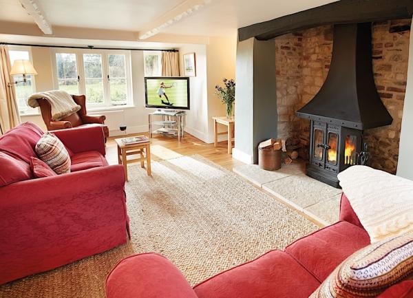 Dorset cottage lounge with 2 matching sofas and armchair, TV and a large inglenook fireplace containing a woodburner.