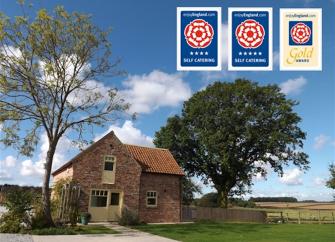 Surrounded by open fields, a barn conversion nestles in front of a large tree in full leaf.