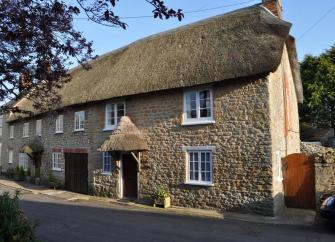 An old stone walled thatched holiday cottage positioned next to a road.
