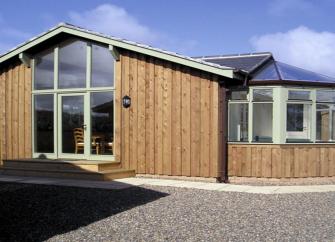 A contemporary wood-clad bungalow with floor-to-ceiling windowsurrounded by a shingled garden.