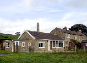 Exterior of a modern bungalow with a conservatory overlooking a grassy field.