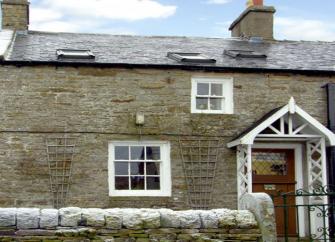 A terraced stone cottage with a low wall around the front garden