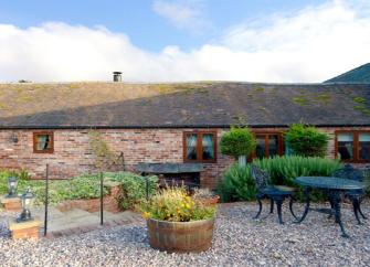A single-storey barn conversion overlook a shingled courtyard with a shrub-filled flower bed.