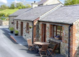A single storey, Gwynedd barn conversion in a courtyard with outdoor tables and chairs.
