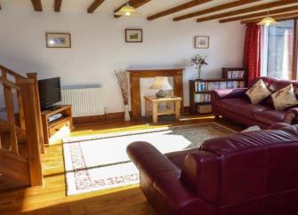 Interior of a spacious pine-floored lounge with pine beams, rugs and large sofas.