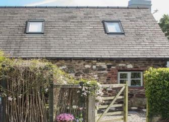 A brick-built barn conversion in Shropshire sits behnd a hedge and a tall, rose covered picket fence