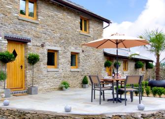 A stone-built Wye Valley holiday cottage overlooks a paved patio with dining furniture.