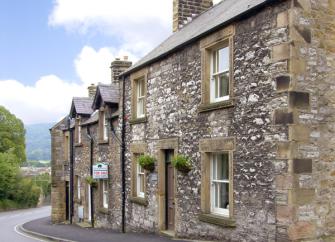 a double-fronted, stone-built terraced cottage on an empty street.