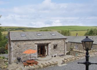 Front exterior of a stone-built barn conversion in Cumbria with a small, paved courtyard.
