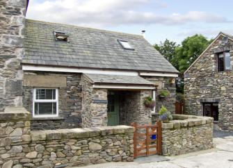 A 2-storey holiday cottage in Ulverston in a converted stone barn surrounded by a low stone wall.