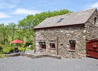 A garden table with a parasol sits outside a stone-built barn conversion in Cumbria.