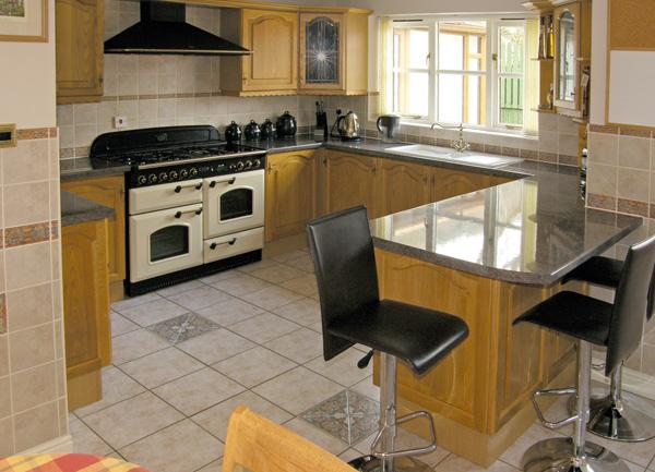 A fitted kitchen with floor and wall mounted units, twin oven and breakfast bar with high stools.