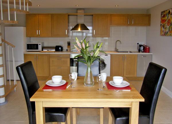 A dining table laid for tea for two with a fitted kitchen behind.