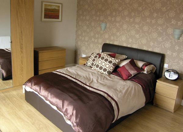 A double bed with twin bedside cabinets, bedside lights and a chest of drawers.
