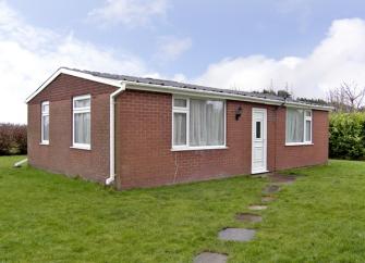 A single storey bick-built bungalow is surrounded by a lawn lined by hedges.