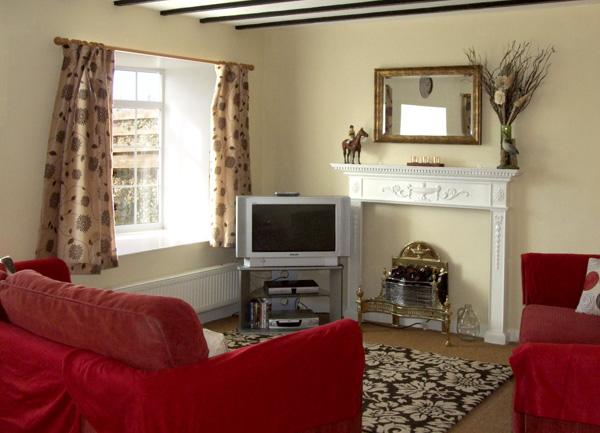 A beamed lounge with a sofa, armchair TV and an ornamental fireplace