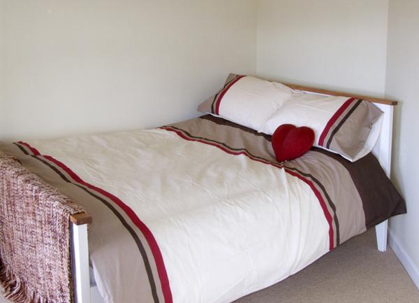 A double bed with a heart-shaped pillow in the corner of a bedroom