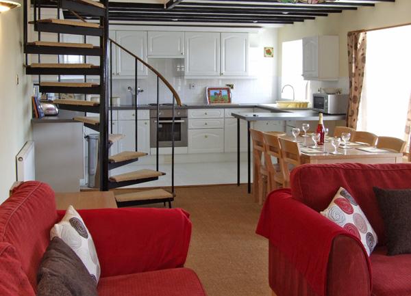 Open plan living area showing a lounge with a spiral staircase, dining and kitchen areas.