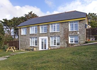 A long, 2-storey stone house overlooks a sloping lawn with a picnic table.