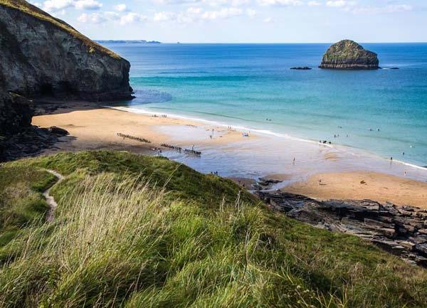 A North Cornwall sandy beach at low tide surrounded by cliffs. A small rocky island lies offshore.
