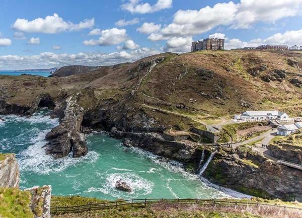 A grand clifftop hotel overlooks rugged cliffs to a rough sea with waves crashing on rocks.