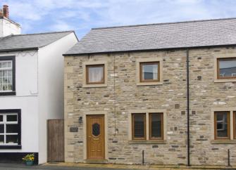 A stone-built, end of terrace cottage overlooking an empty street.