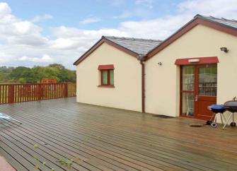 Twin gabled exterior of a bungalow with a feenced-in, large wooden deck for BBQs surrounding it.