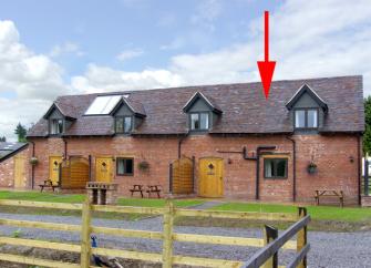 An end-of-terrace, brick holiday cottage in Church-Stretton behind a front lawn.