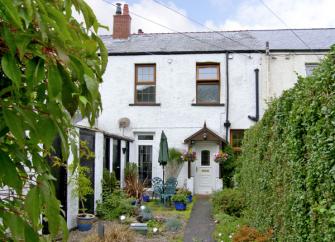 A 2-storey, stone-built gwynedd holiday covvage oveerlooks a garden full of poptted plants and shrubs.