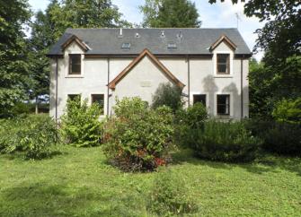 A double-fronted holiday cottage witha covered porch overlooks a mature front garden.