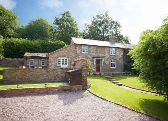 A stone-built Herefordshire cottage overlooks a tree-lined lawn and parking space.