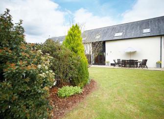 A barn conversion with Velux windows in the roof overlooks a large lawn.