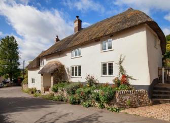 Front exterior of a thatched Devon longhouse on a quiet Devon lane.