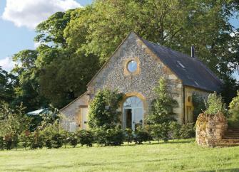 A coach house conversion with tall trees behind and a lawn in front.