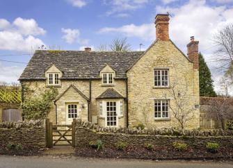 Cotswold cottage exterior with a bay window and low stone garden wall.