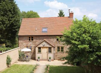 A stone-built cottage with enclosed porch overlooks a secure lawned garden