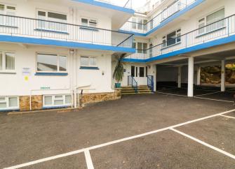 Exterior of an L-shaped apartment building with iron-railings protecting walkwabys and spaced for parking beneath.