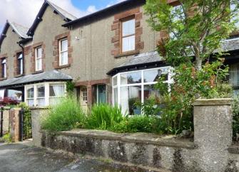 A 2-storey, terraced house with a large groundfloor bay window and a shrub-filled front garden.