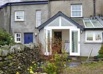 Rear exterior of a terraced holiday cottage in Ulverton overlooking a garden with flowering bulbs.