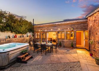 A wood-clad, single-storey Quantock Hills holiday home overlooks a courtyard with a hot tub at dusk.