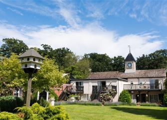 A 2-storey house with a central clocktower and a long 1st-floor deck overlooking a spacious lawn.