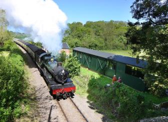 A stem engines rushes through Somerset countryside past two old carriages converted to holiday homes