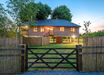 House lights in this wooden Somerset holiday cottage glow brightly in the dusk.