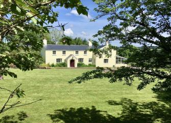 An Exmoor farmhouse overlooks a large lawn surrounded by trees.
