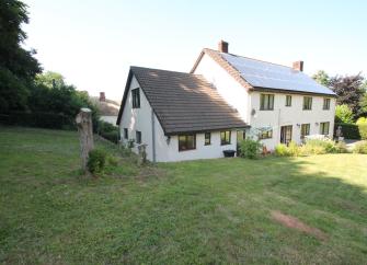 A two storey cottge with a modern extension in Monksilver is surrounded by large, hedge-lined lawns