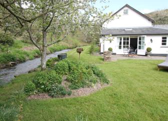 A country cottage with a large lawn overlooks a large stream.