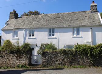 Quaint country cottage overlooks a garden surrounded by a stone wall.