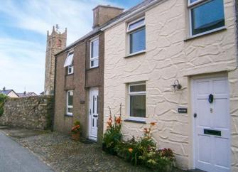 A rendered holiday cottage overlooking a quiet lane near a church tower.