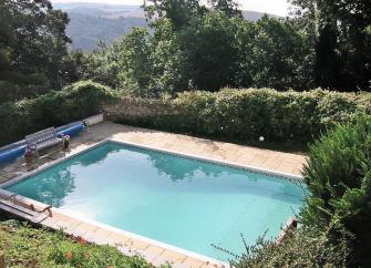 An open air swimming pool with park benches on its terrace surrounded by a tall hedge.